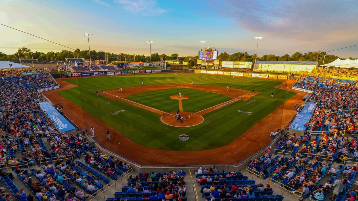 A full minor league ballpark at dusk with the lights on