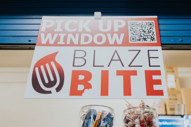 A red Pick Up Window BlazeBite sign with a QR code above a counter