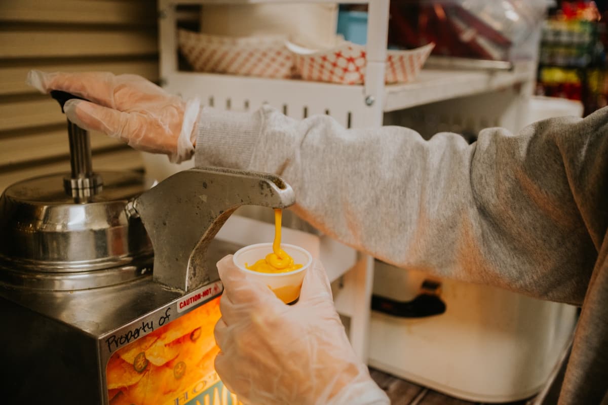 A volunteer pumping cheese into a cup at the stand
