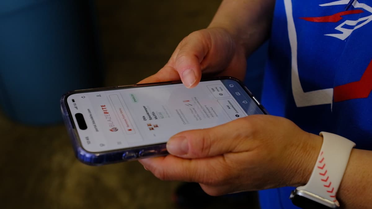 A fan holding a phone with the BlazeBite menu open on a game day