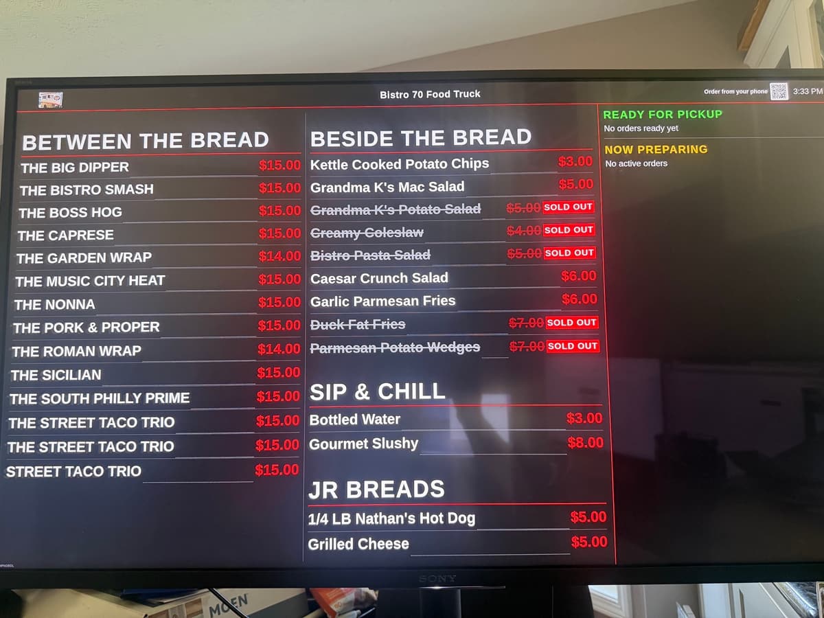The Bistro 70 food truck menu on a BlazeBite board on a TV, with sold-out items struck through and the order status column on the right