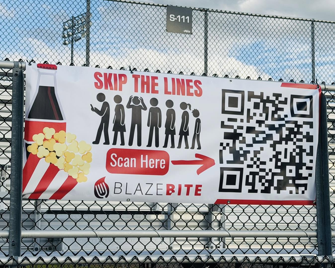 A "Skip the Lines — Scan Here" BlazeBite banner zip-tied to a stadium fence
