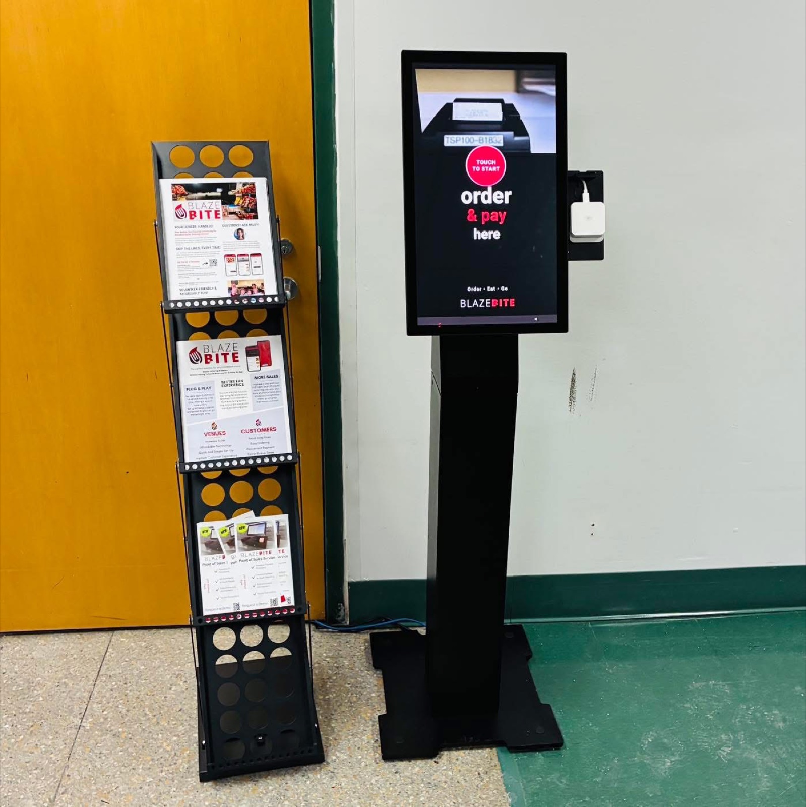 A BlazeBite kiosk on its floor stand in a school hallway, next to a rack of brochures