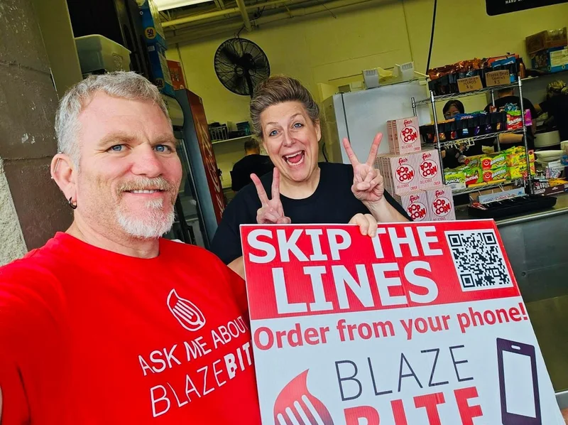 Two concession volunteers holding a "Skip the lines, order from your phone" BlazeBite sign